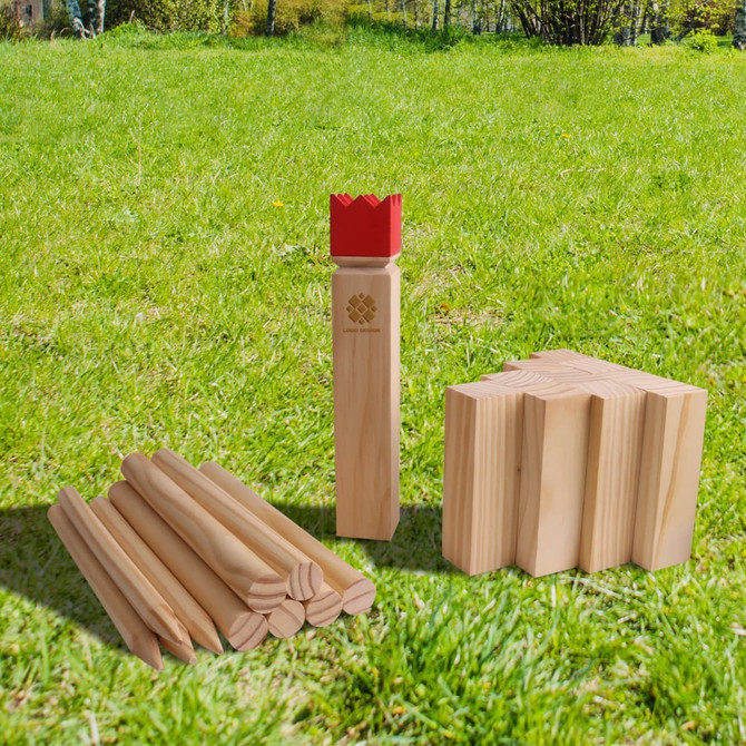 A Premium Wooden Kubb Set featuring natural wood pieces with one red crown piece, set on green grass.