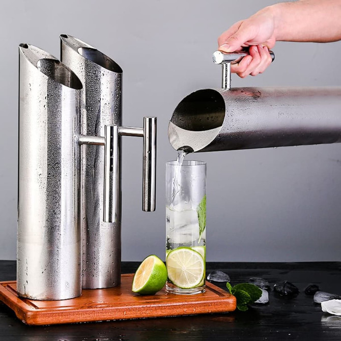 A stainless steel pitcher with a sleek design, pouring a drink into a glass filled with ice and lime.