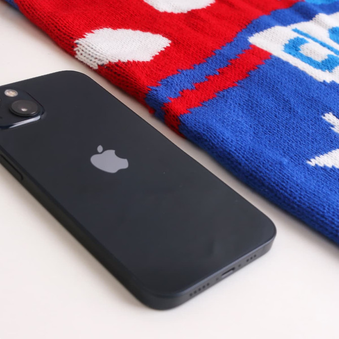 A black smartphone lies next to a red and blue Jacquard sweater featuring a pattern and logo.