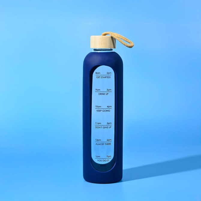 A drink bottle in navy blue with a cream lid and a carrying strap. It features a branded logo and time markers.