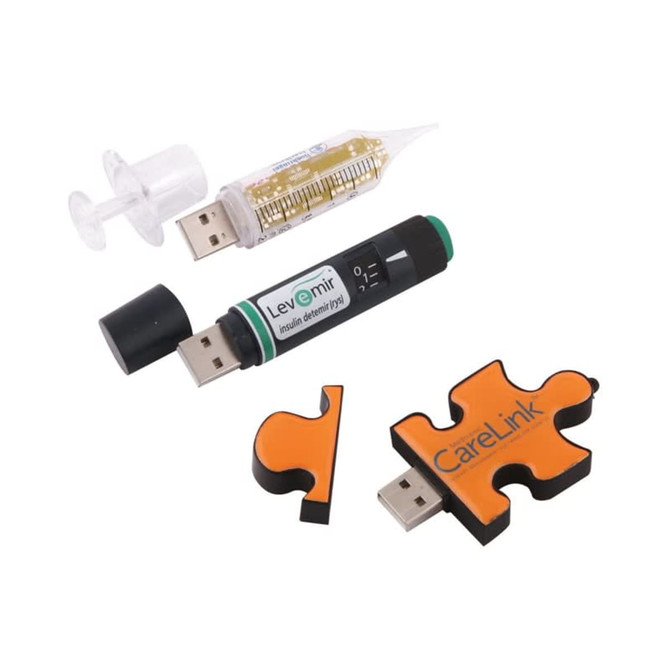 Three USB flash drives in various shapes: a syringe, an insulin pen, and a puzzle piece, featuring black, green, and orange colours.