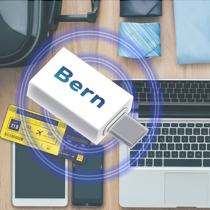 A Type-C to Type-C data blocker in white, surrounded by a laptop, phone, travel tickets, and a blue tie.
