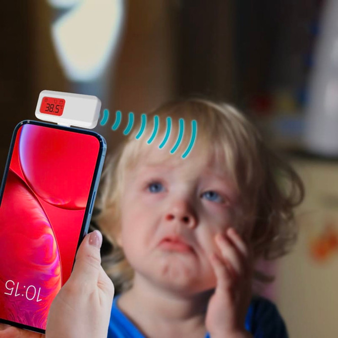 A smartphone with a white thermometer attachment displays a temperature reading near a child with a distressed expression.