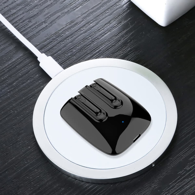A pair of black magnetic TWS earbuds resting on a round charging pad on a wooden surface.