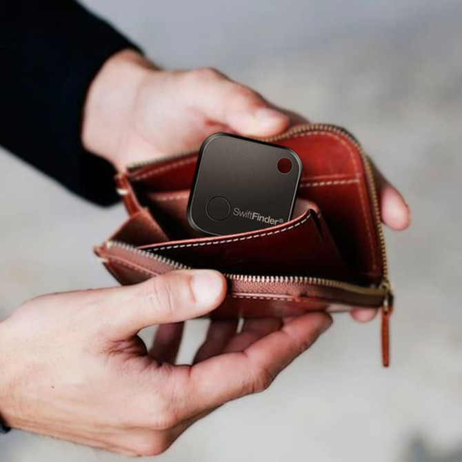 A black SwiftFinder Smart Tag Tracker inside a brown wallet, held by a person’s hands.