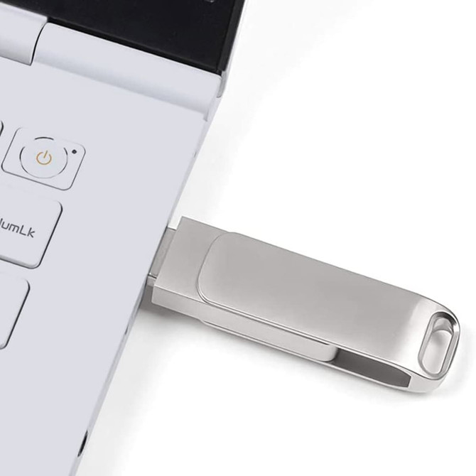 A silver USB flash drive is plugged into the side of a laptop, showcasing its sleek design.