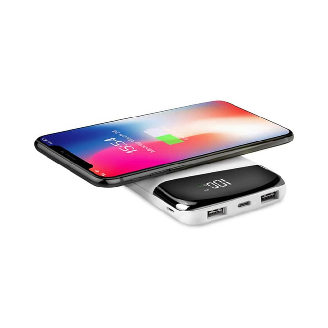 A wireless power bank in white with two USB ports, charging a smartphone. The smartphone displays a battery charging indicator.