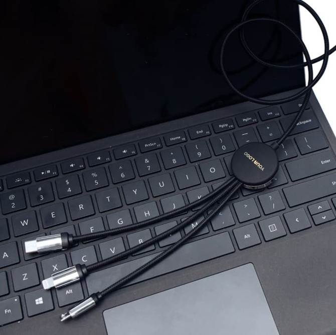 A black charging cable with multiple connectors lies on a laptop keyboard. The cable features a circular connector with branding.