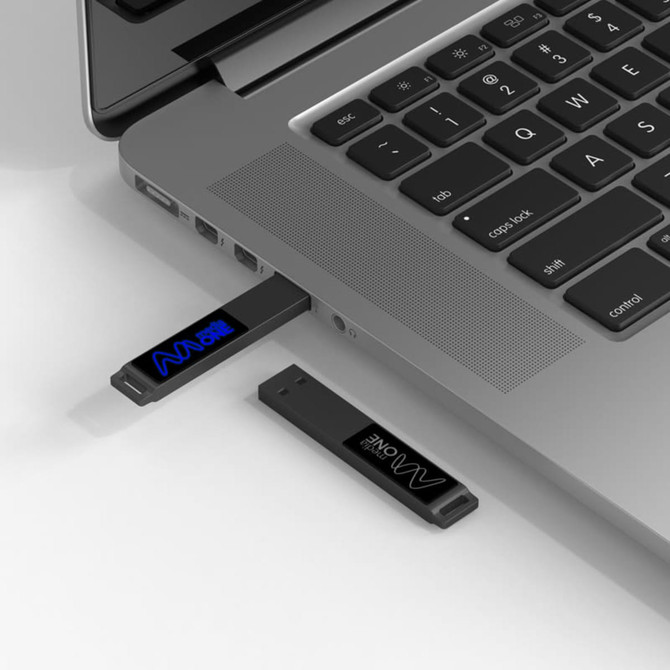 A black LED flash drive is connected to a laptop USB port, displaying a light feature. The laptop has a grey finish.
