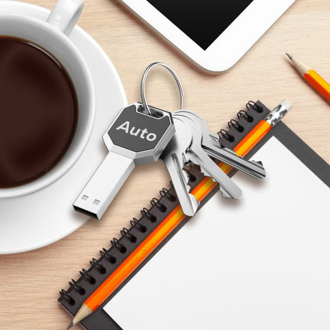 A silver key-shaped USB flash drive rests on a desk beside a coffee cup, notebook, and stationery.