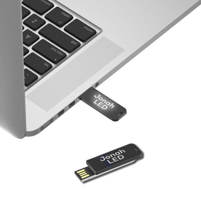 A black Jonah LED clip flash drive partially inserted into a laptop USB port, showcasing its sleek design.