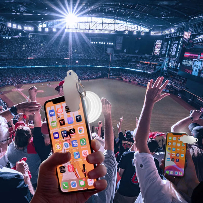 A smartphone with a white torch attachment, held by a person in a crowd at a sports event, surrounded by cheering fans.