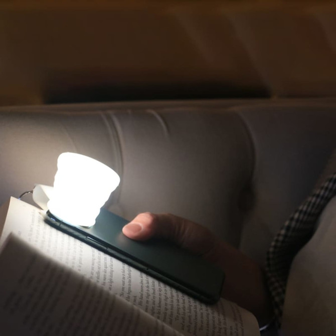 A compact white torch attached to a smartphone, illuminating a book in a dimly lit setting.