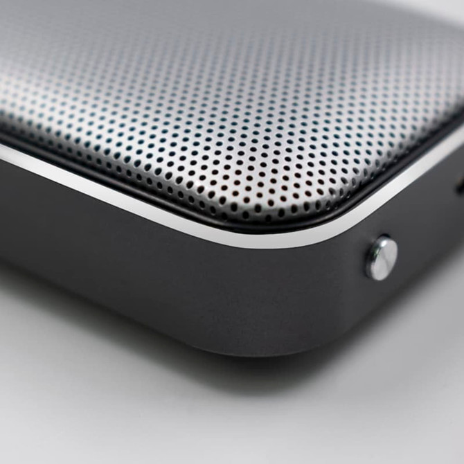A silver and black Bluetooth speaker with a perforated surface and smooth edges, featuring a small button on the side.