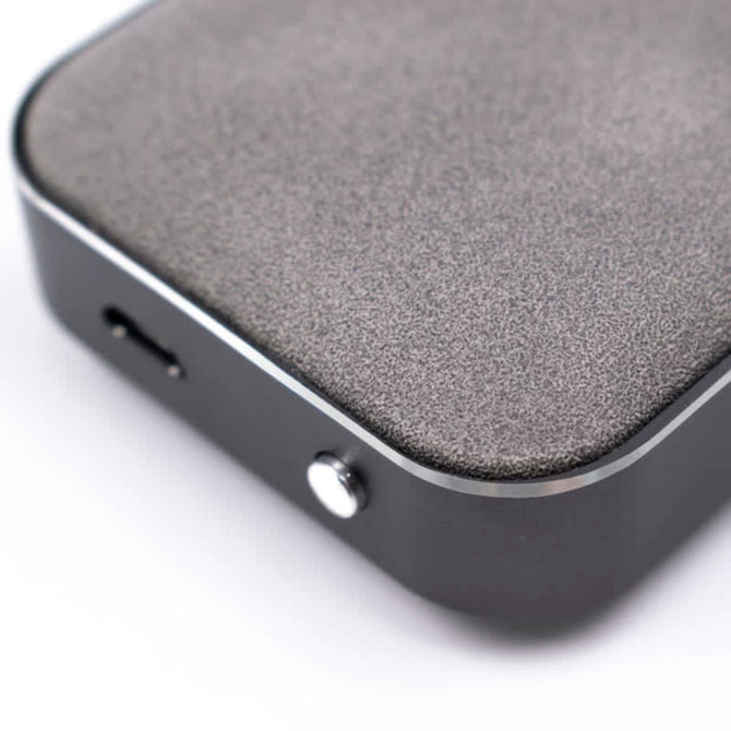 A Bluetooth speaker with a matte grey surface and a shiny black edge, featuring a charging port and a button.