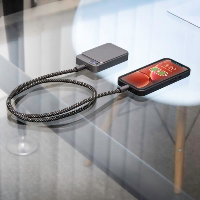 A black magnetic wireless power bank connected to a phone on a glass table. The power bank has a sleek design.