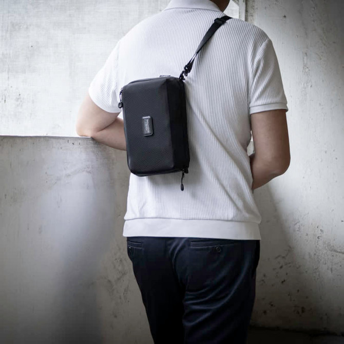 A black toiletry bag is worn crossbody by a person, showcasing its sleek design and compact size.