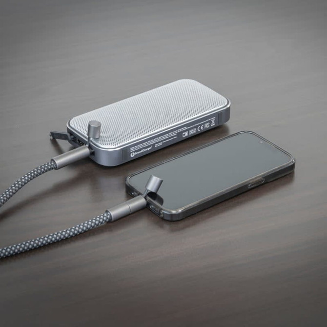 A silver Bluetooth speaker power bank connects to a black smartphone, resting on a wooden surface.