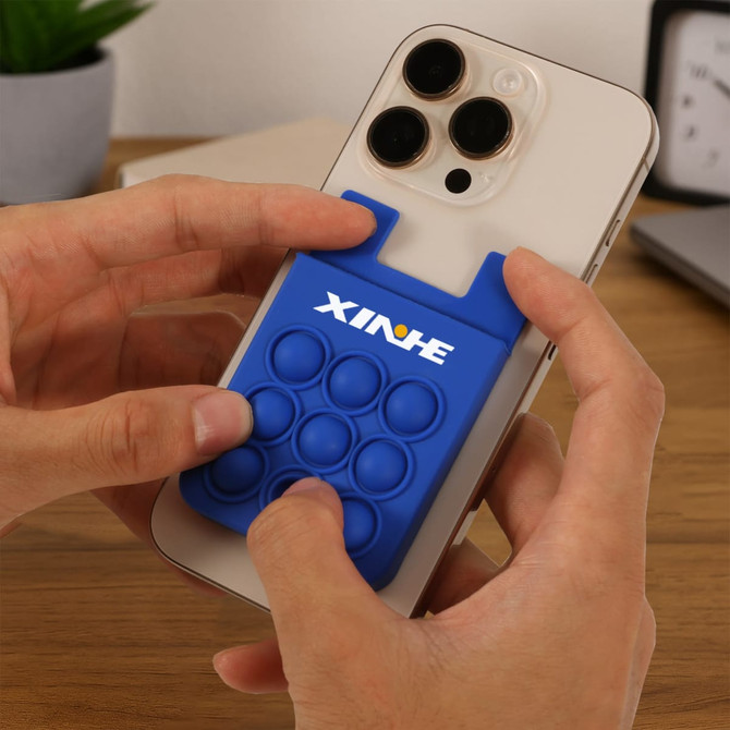 A blue silicone phone wallet featuring a pop design, attached to a smartphone being held by hands.