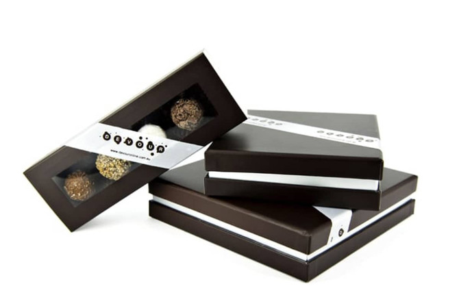 A stack of three dark chocolate boxes with transparent windows, showcasing assorted chocolates inside. Each box is elegantly tied with a ribbon.