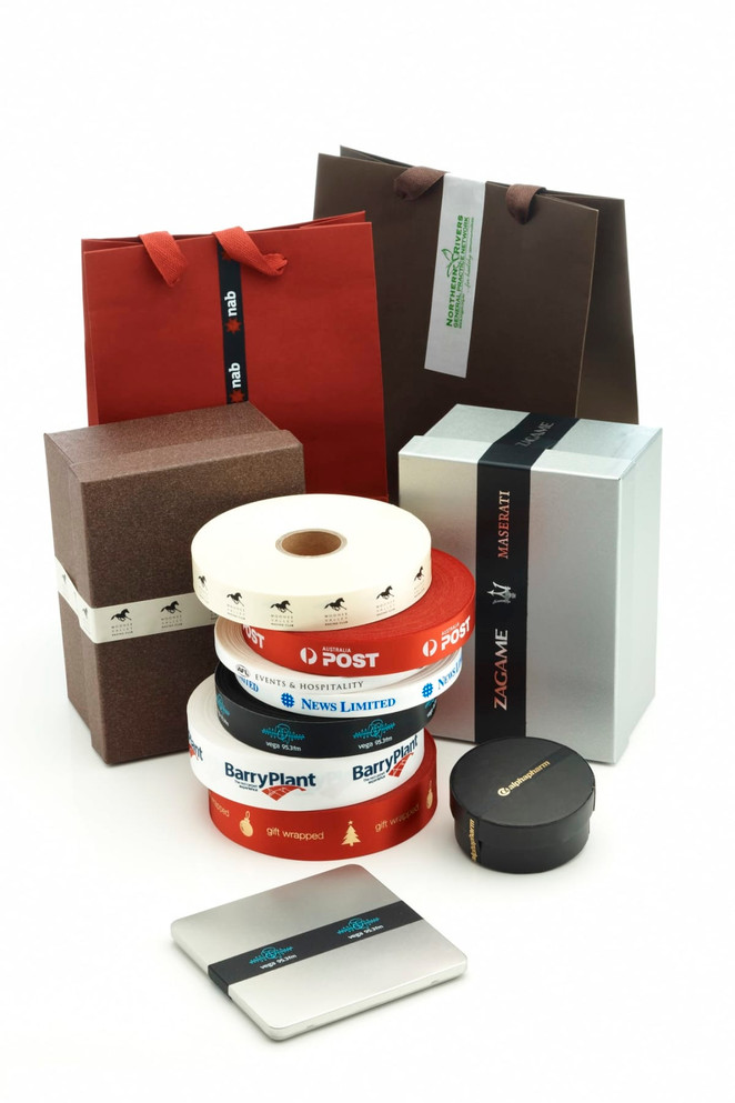 A collection of gift boxes and bags in various colours, featuring custom printed satin ribbons in red, white, and black.