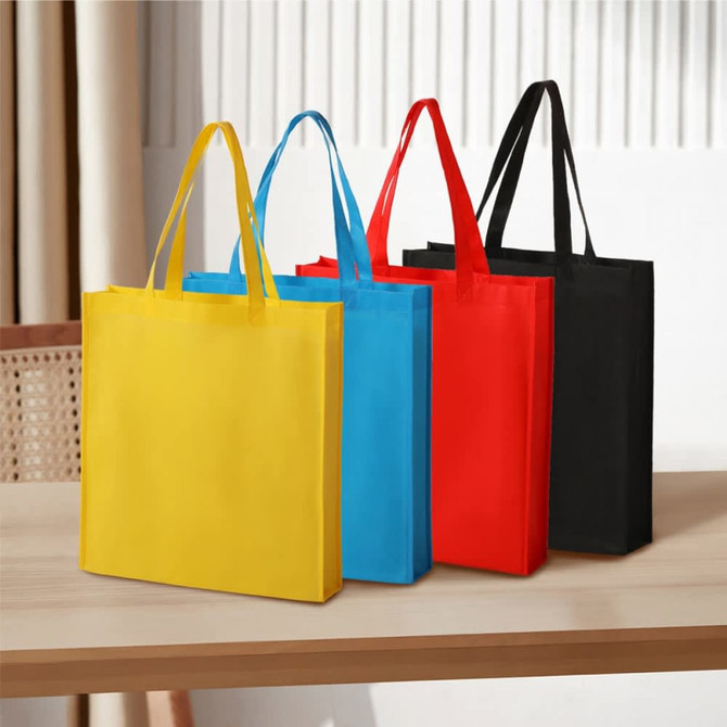 A selection of four tote bags in yellow, blue, red, and black, displayed on a table against a light background.