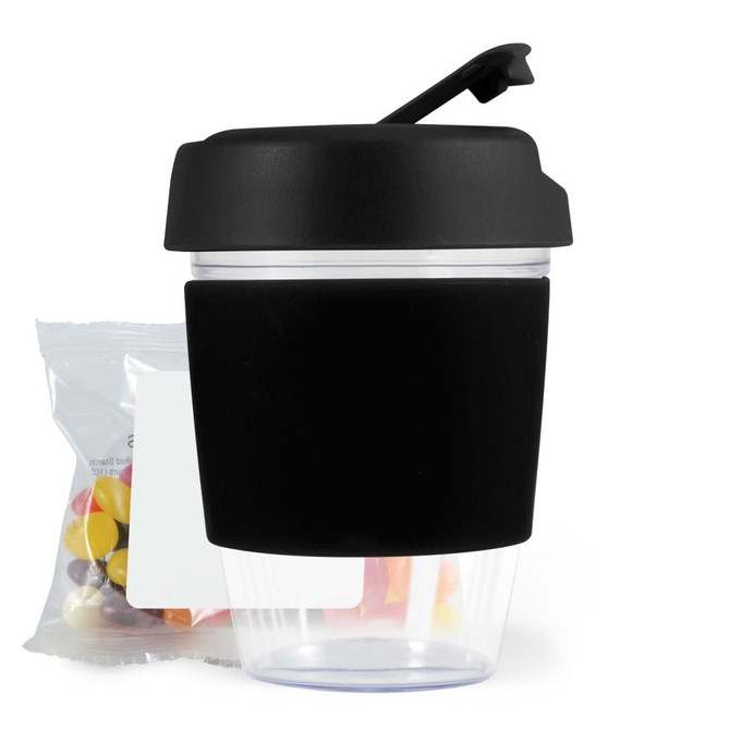 A reusable coffee cup with a black silicone sleeve and a secure lid, accompanied by a pack of colorful jelly beans.