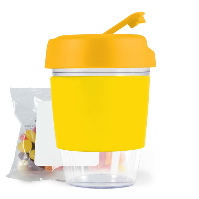 A reusable coffee cup in bright yellow with a matching lid and a clear base, accompanied by a pack of jelly beans.