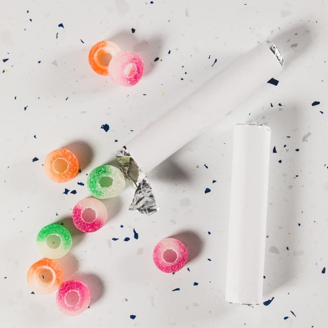 Assorted fruit-flavoured gummy rings in various colours, scattered around a partially unwrapped roll.