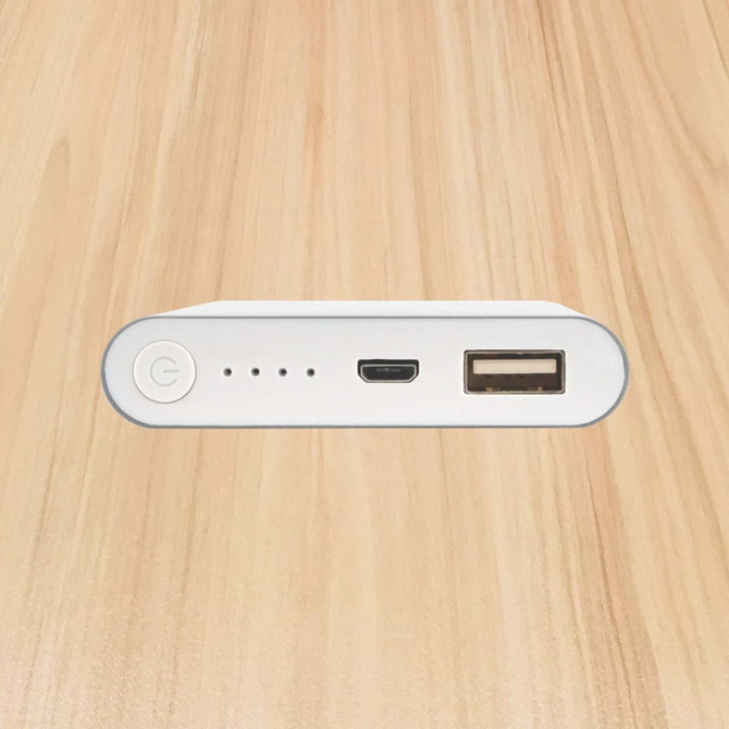 A white power bank with a USB port, a micro USB port, and indicator lights on a wooden surface.