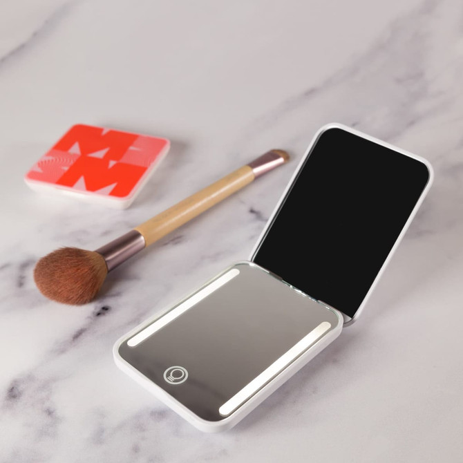 A white LED compact mirror with a reflective surface, next to a makeup brush and a compact case.