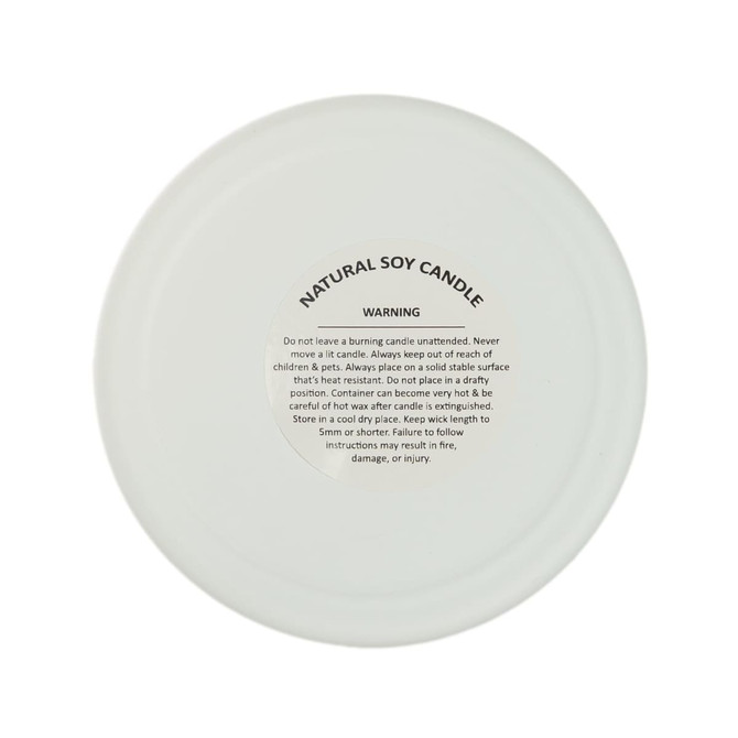 A natural soy candle with a warning label on the bottom, detailing safety instructions.