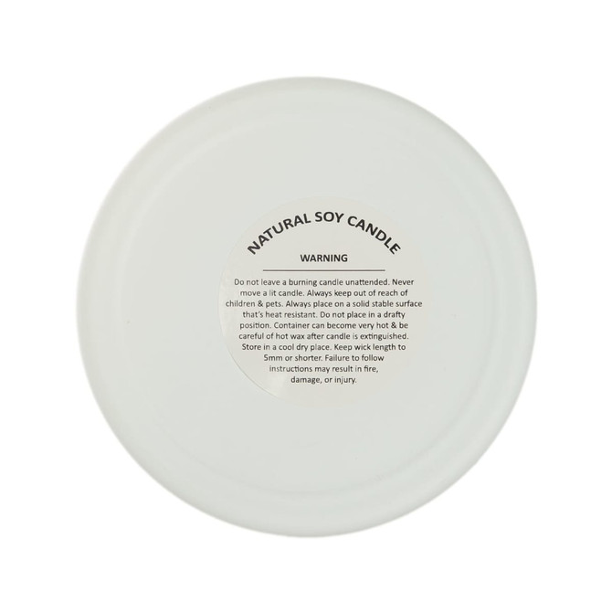 A large white glass candle with a frosted finish and a warning label on the base, featuring natural soy wax.