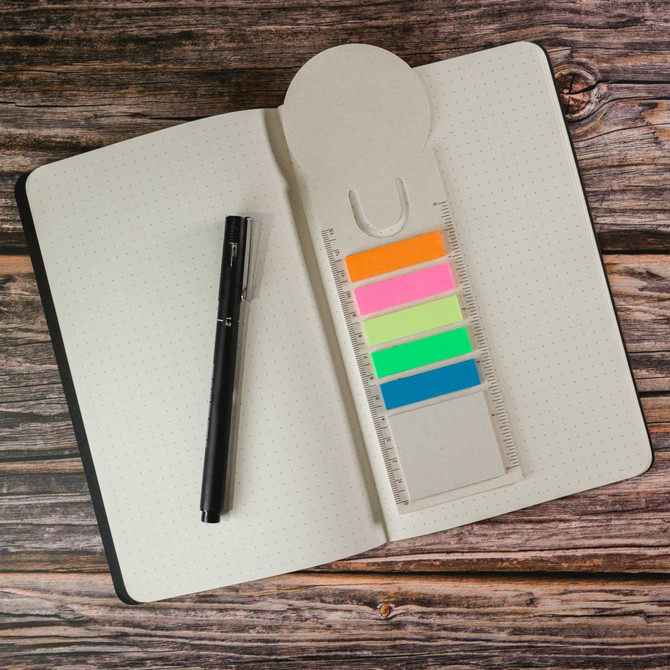 A milk carton-shaped bookmark with colorful sticky tabs and a ruler, placed inside a notebook alongside a black pen.