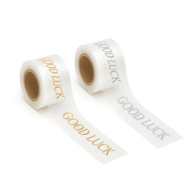 Two rolls of promotional soft ribbon in white, featuring "Good Luck" printed in gold and silver text.