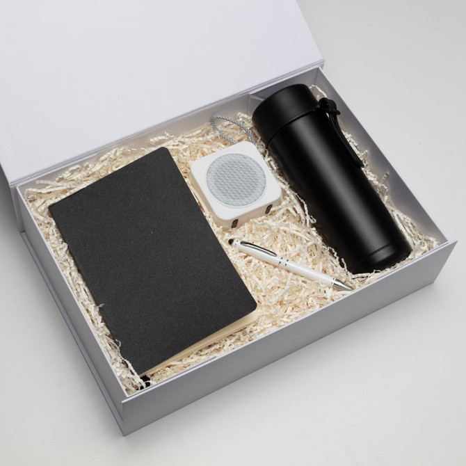 A black drink bottle, a notebook, a white speaker, and a pen packed in a gift box with shredded paper.