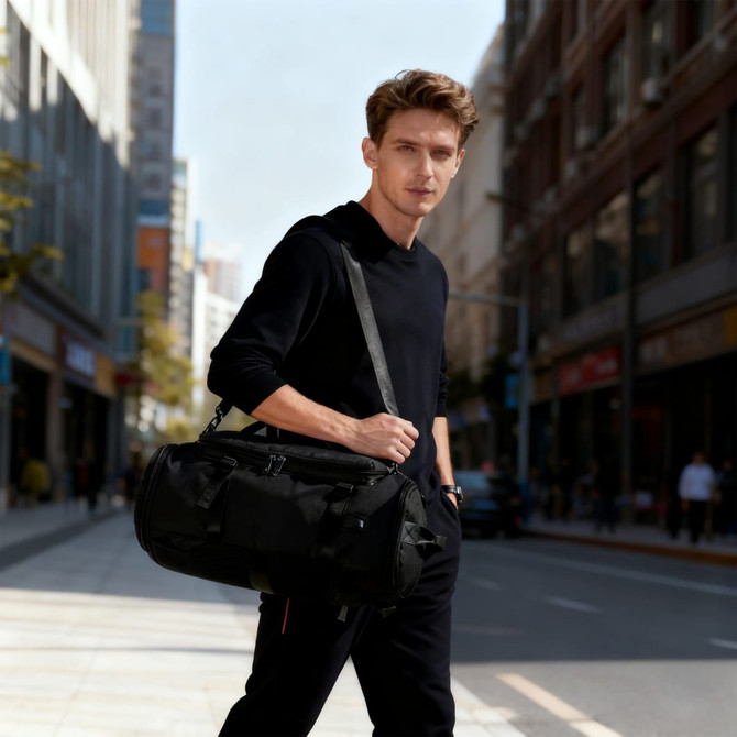A black convertible bucket backpack duffel bag is held by a man standing on a city street. The bag features a logo.