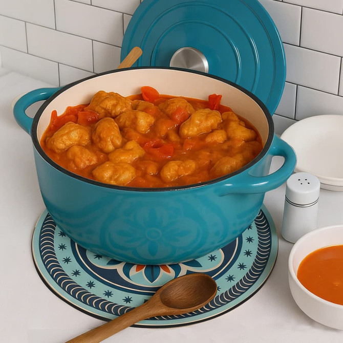 A turquoise pot filled with dumplings and red peppers sits on a decorative trivet, accompanied by a wooden spoon and a bowl.