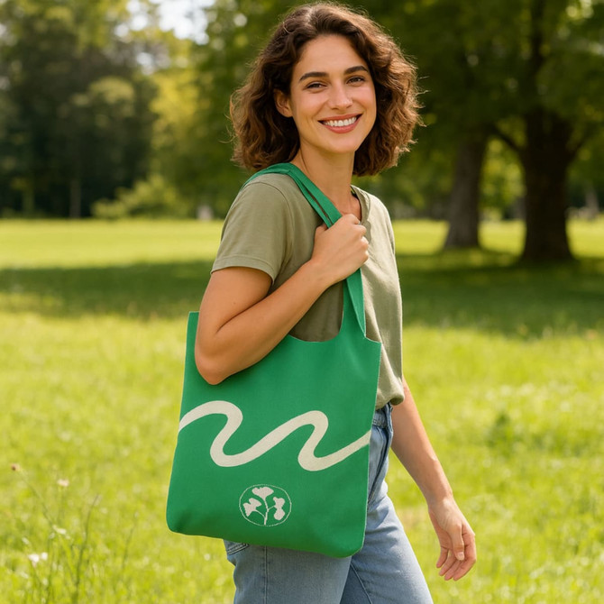 A green large capacity knitted shoulder bag being carried by a smiling person in a grassy park setting.