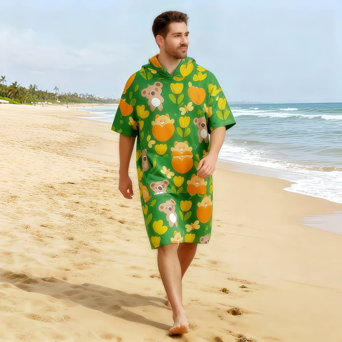 A green hooded towel poncho featuring floral and animal patterns, worn by a man on a sandy beach.