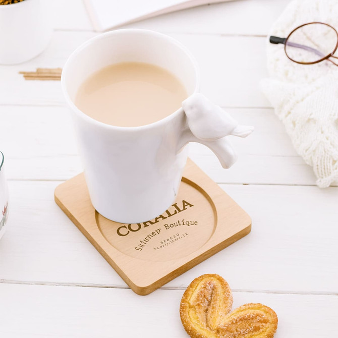A wooden coaster with a square shape and circular center, featuring a light brown finish. It has a logo.