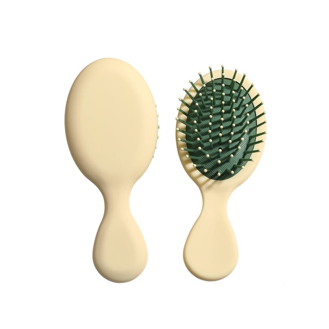 A mini paddle brush with a cream handle and green bristle base, featuring a logo on the handle.