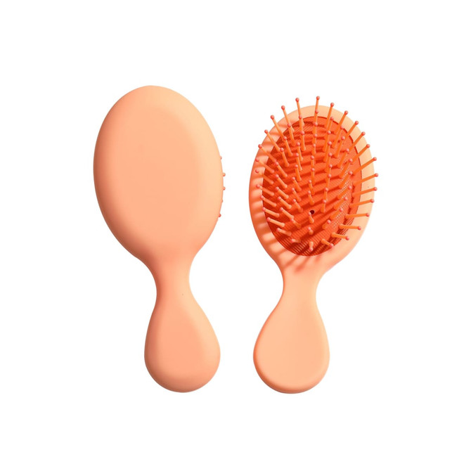 A mini paddle brush in a soft peach colour with plastic bristles and an ergonomic handle. It has a simple logo.