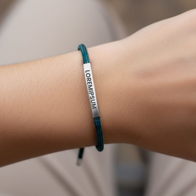 A metal woven bracelet with a silver plate on a green cord, worn on a wrist.