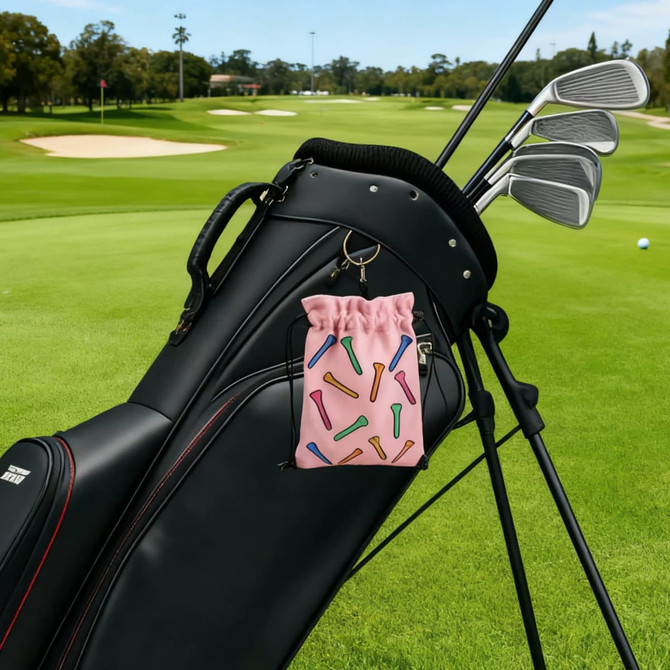 A pink pouch with colourful designs attached to a black golf bag, with golf clubs in view against a green course backdrop.