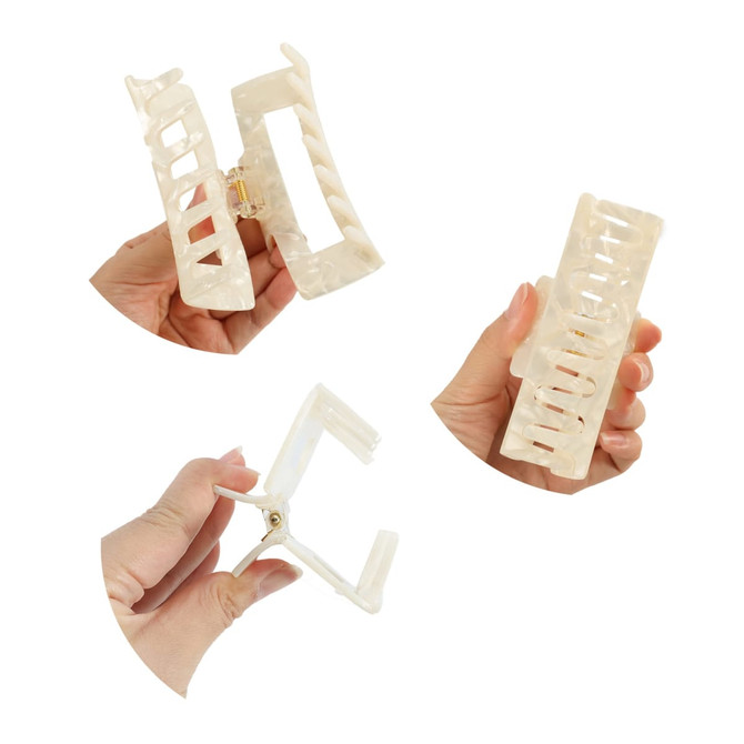 A hair claw clip in a marbled white design, being held in a hand, showcasing its open and closed positions.