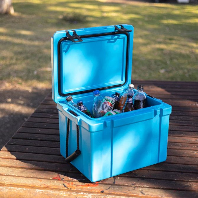 A blue 25L cooler box is filled with various soft drink bottles and water bottles, sitting on a wooden surface.