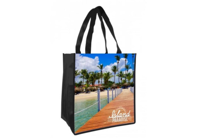 A black tote bag featuring a full-colour print of a beach scene with palm trees and a wooden walkway.