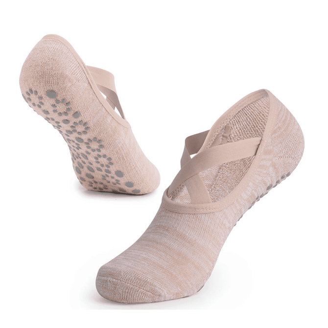 A pair of beige yoga socks featuring a cross-strap design and a textured grip sole.