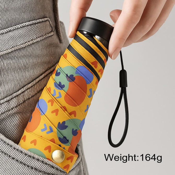 A small, lightweight umbrella in a vibrant yellow design with colourful patterns, being held in a pocket.